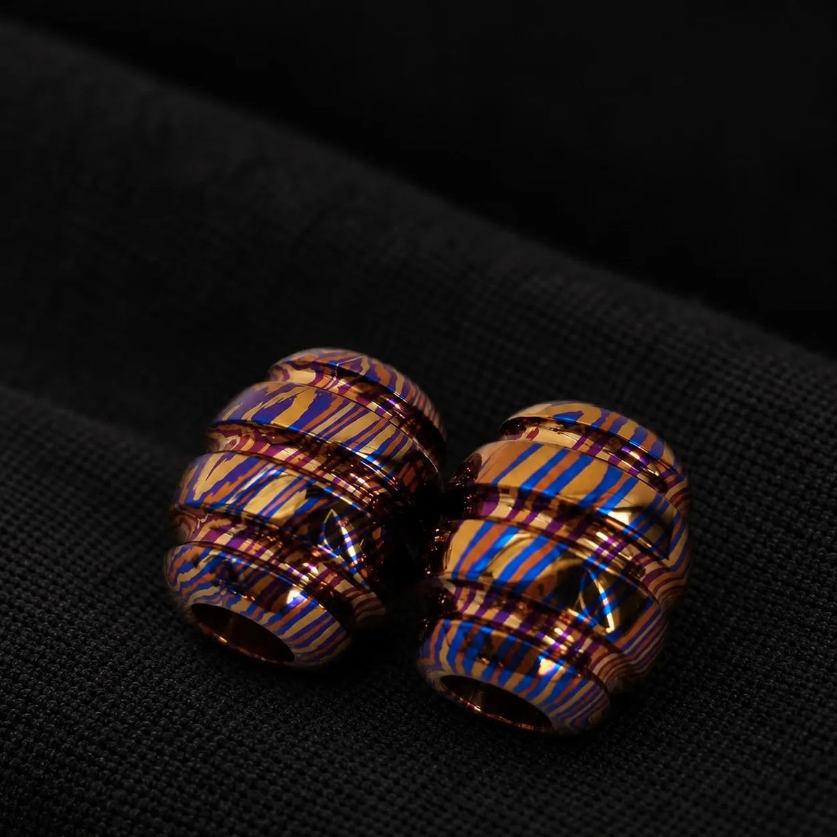 Timascus barrel lanyard bead on black cloth — blue, gold and purple grain