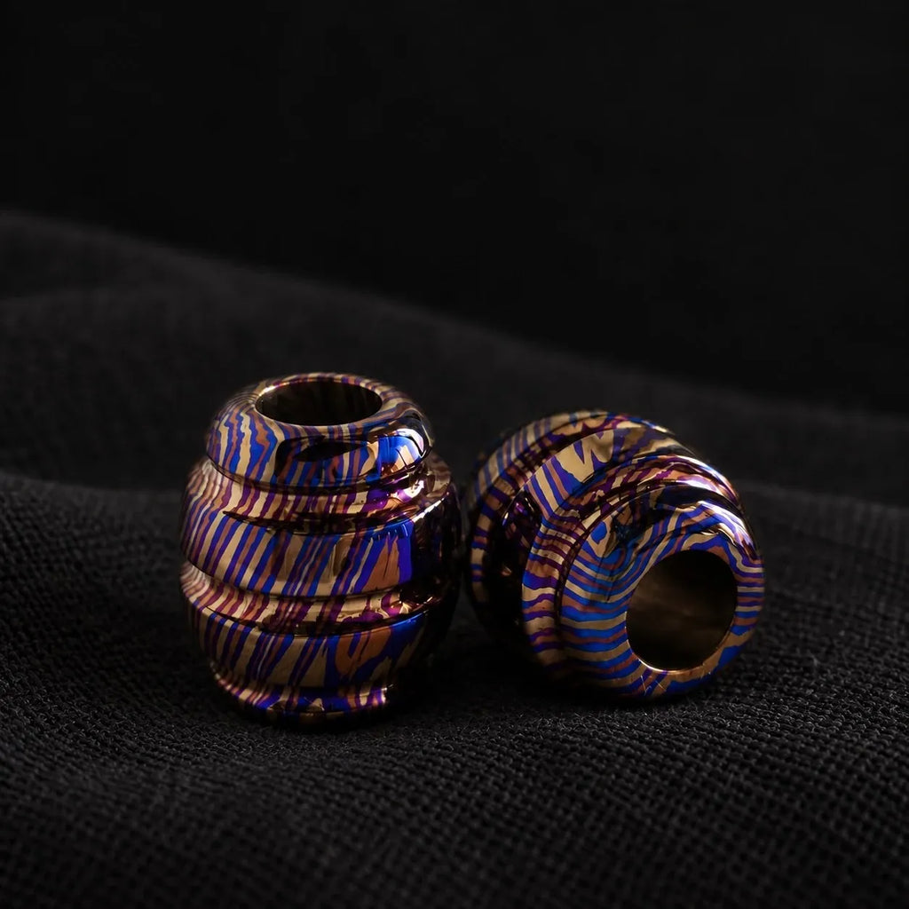Timascus bead upright showing the through-hole, one lying flat, on black cloth