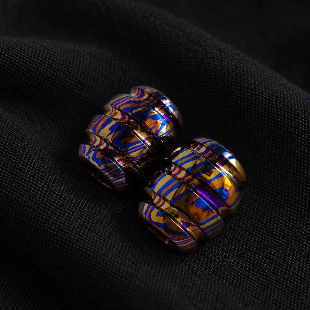 Two Timascus beads showing how the grain wraps the barrel, on black cloth
