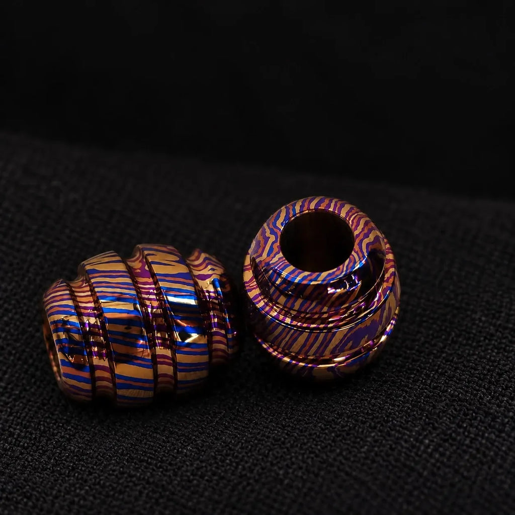 Timascus bead on its side next to an upright bead, on black cloth